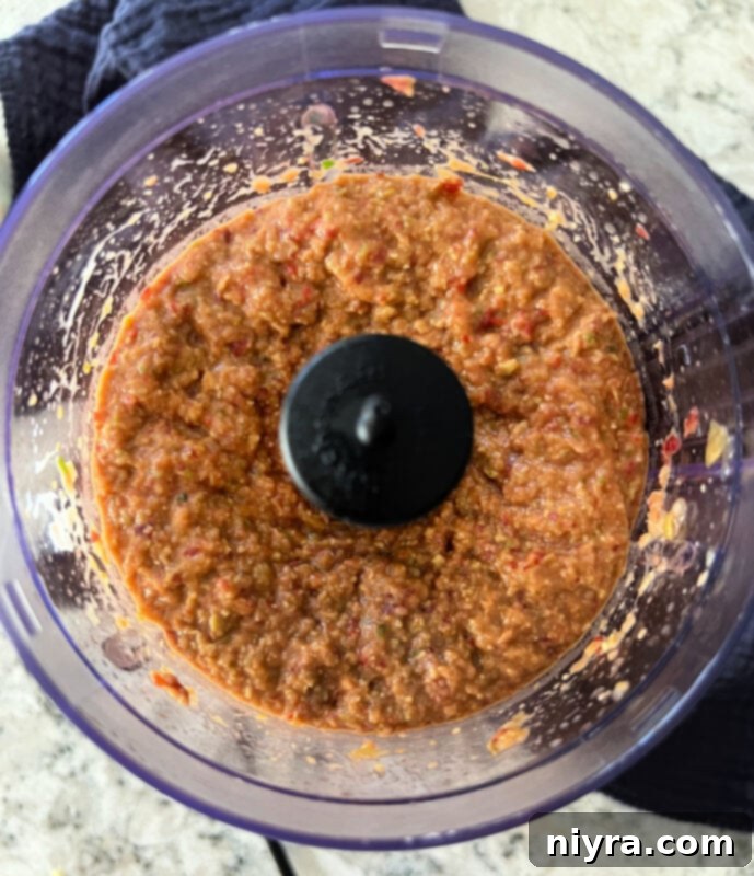 Step 2: The food processor is actively blending the Asian Bean Dip ingredients, creating a smooth, creamy texture. The sides of the bowl show some unblended bits, indicating it's time to scrape down.