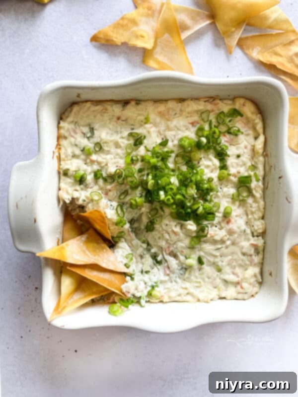 Close-up of baked Crab Rangoon Dip, golden and bubbly, with fresh green onion garnish.