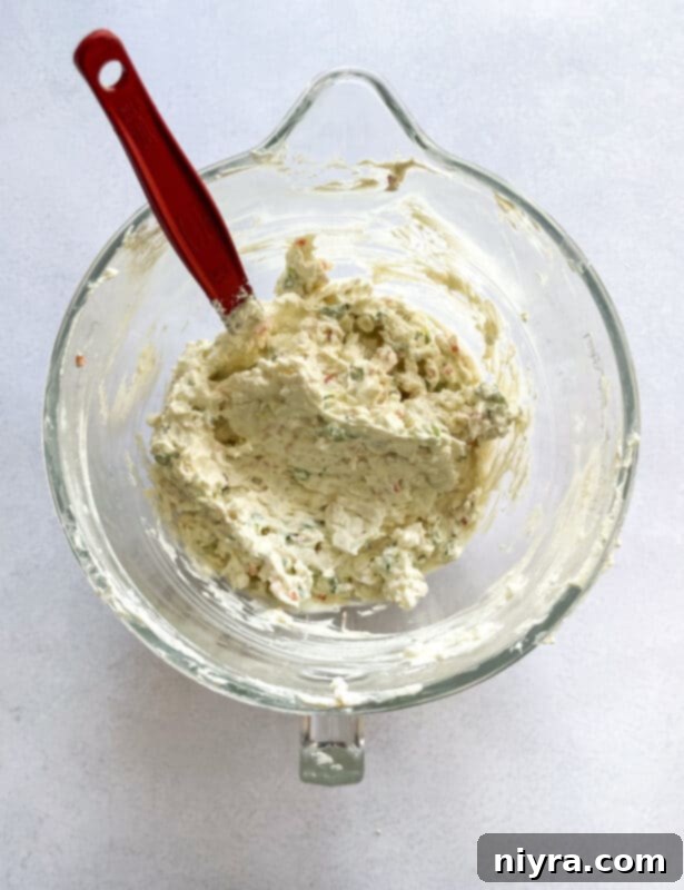 Softened cream cheese being beaten in a bowl with an electric mixer.