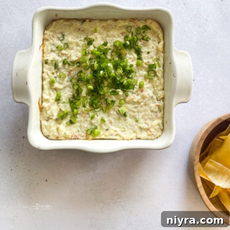 Baked Crab Rangoon Dip in a white dish, garnished with green onions, ready to be served.