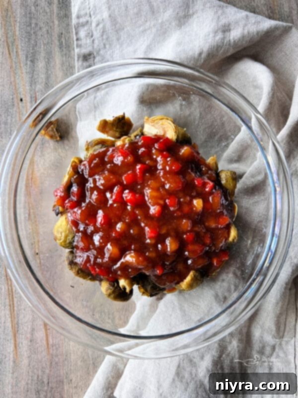 Sweet and sour sauce being poured over air-fried Brussels sprouts