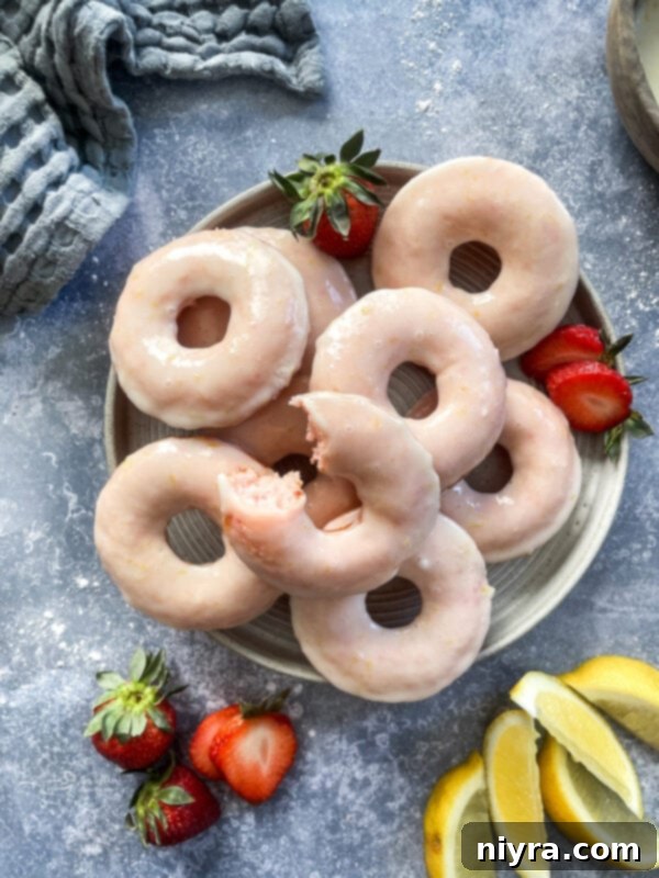 A plate of strawberry lemonade donuts, garnished with lemon slices and fresh strawberries.