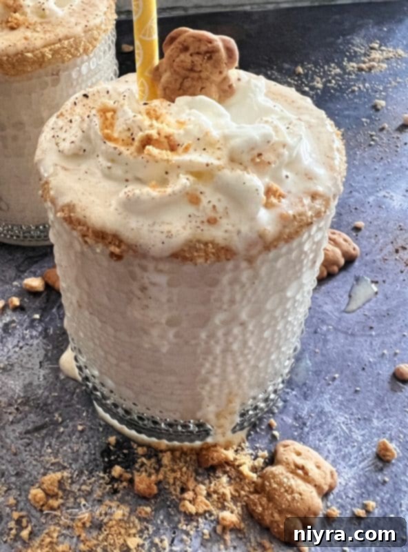 Creamy Banana Cream Pie Shake topped with whipped cream and graham cracker crumbs, in a glass with a straw.