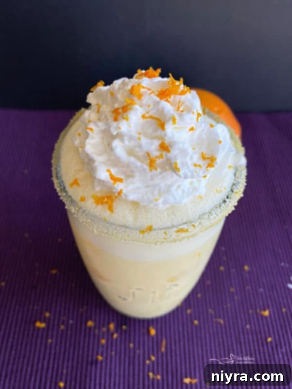 A beautifully garnished Grown-Up Orange Julius cocktail with whipped cream and an orange slice.