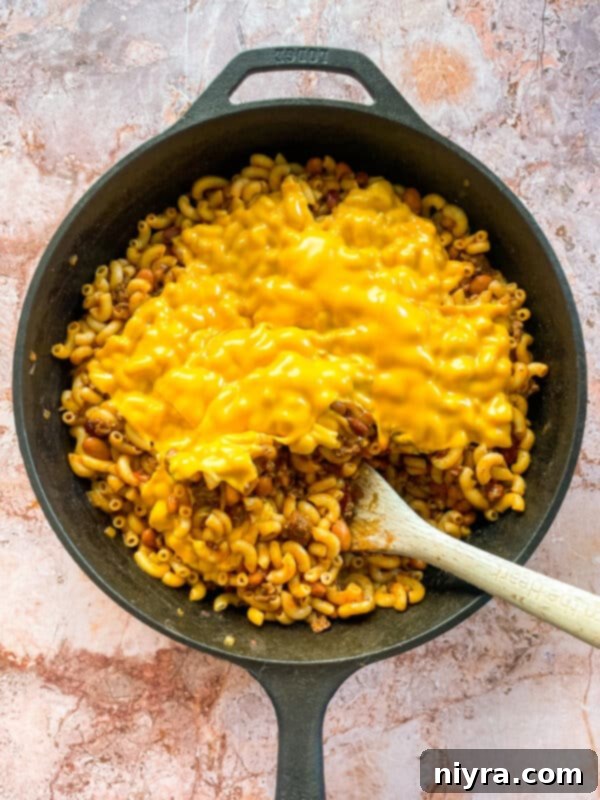 Adding macaroni to the chili mixture in a skillet