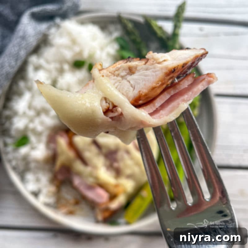 A serving of Smoky Mountain Chicken with a fork, highlighting the melted cheese and ham.