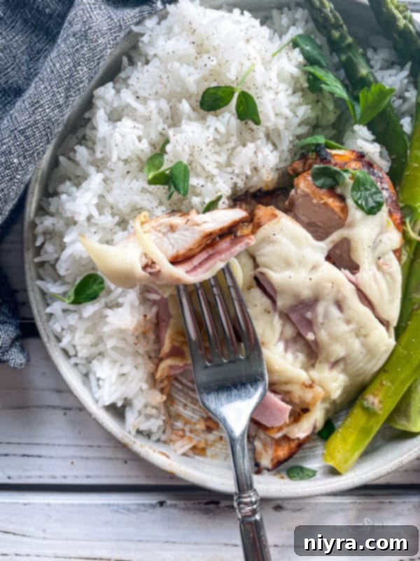 A fork piercing a piece of Smoky Mountain Chicken, showing the layers of cheese, ham, and chicken.