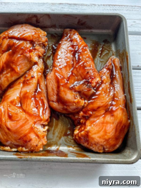 Chicken breasts being coated in BBQ sauce inside a ziplock bag.