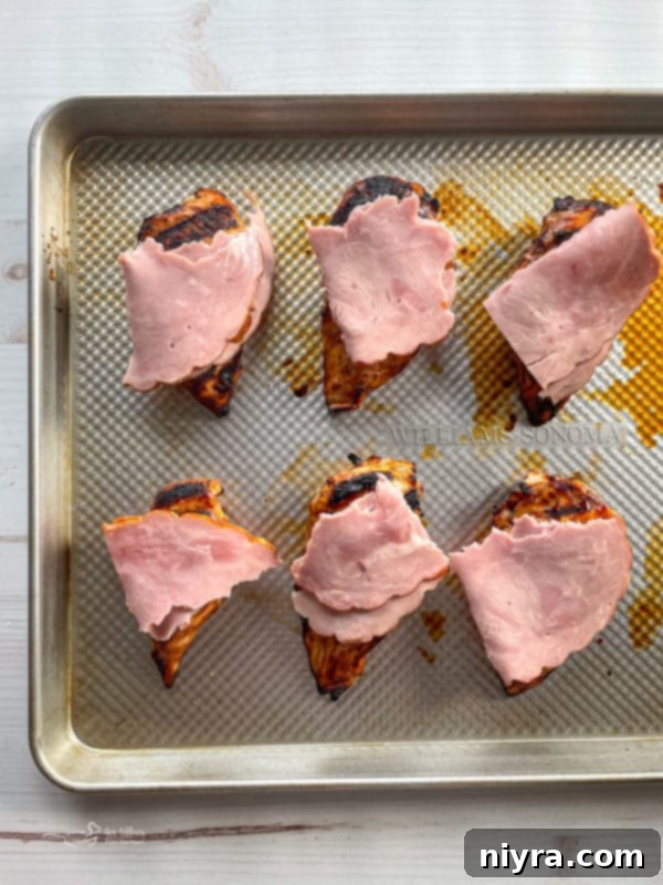 Grilled chicken breasts on a baking sheet, topped with thick slices of ham.