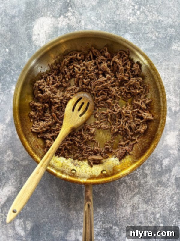 Aunt Sue's Ultimate Doritos Taco Salad 6 Lean ground beef browning in a large skillet, with a wooden spoon breaking it apart.