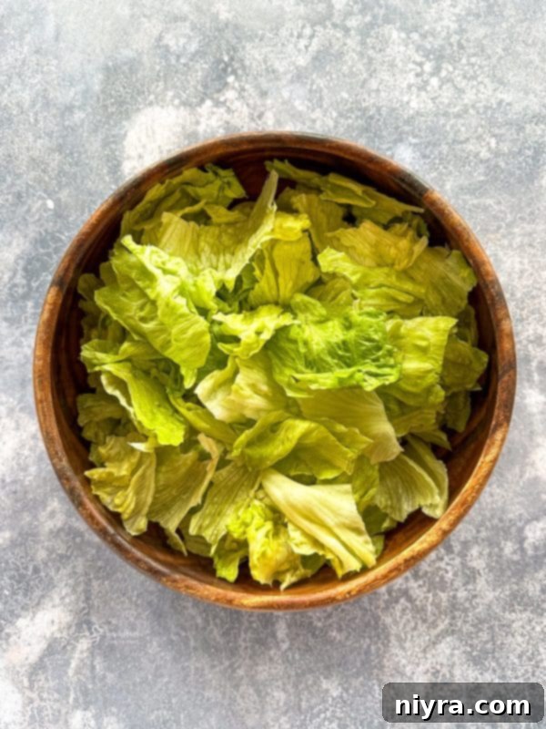 Aunt Sue's Ultimate Doritos Taco Salad 7 A large head of iceberg lettuce being ripped into bite-sized pieces over a large mixing bowl.