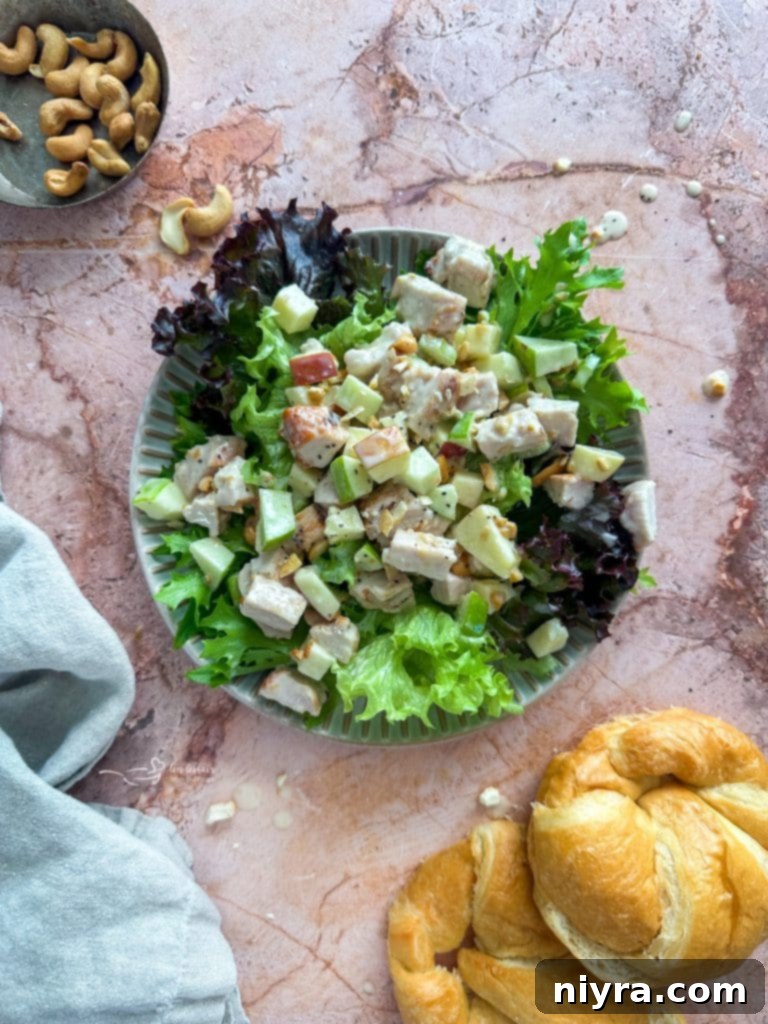 Ingredients for Apple Chicken Salad laid out on a white surface, including cooked chicken, apples, celery, cashews, honey, mayonnaise, and apple cider vinegar.