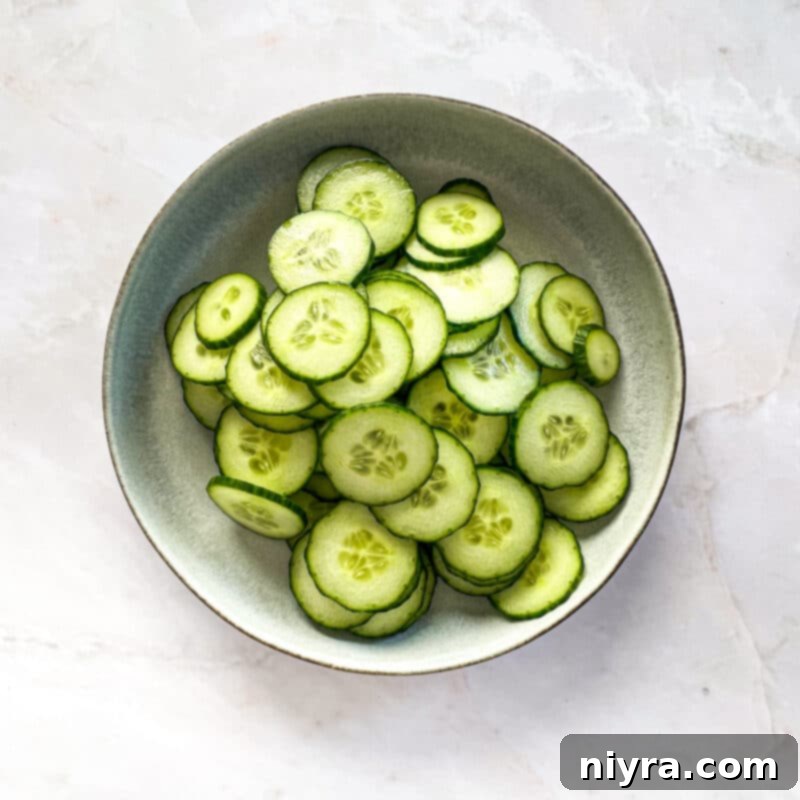 Step 3: Fresh English cucumbers being thinly sliced on a cutting board.