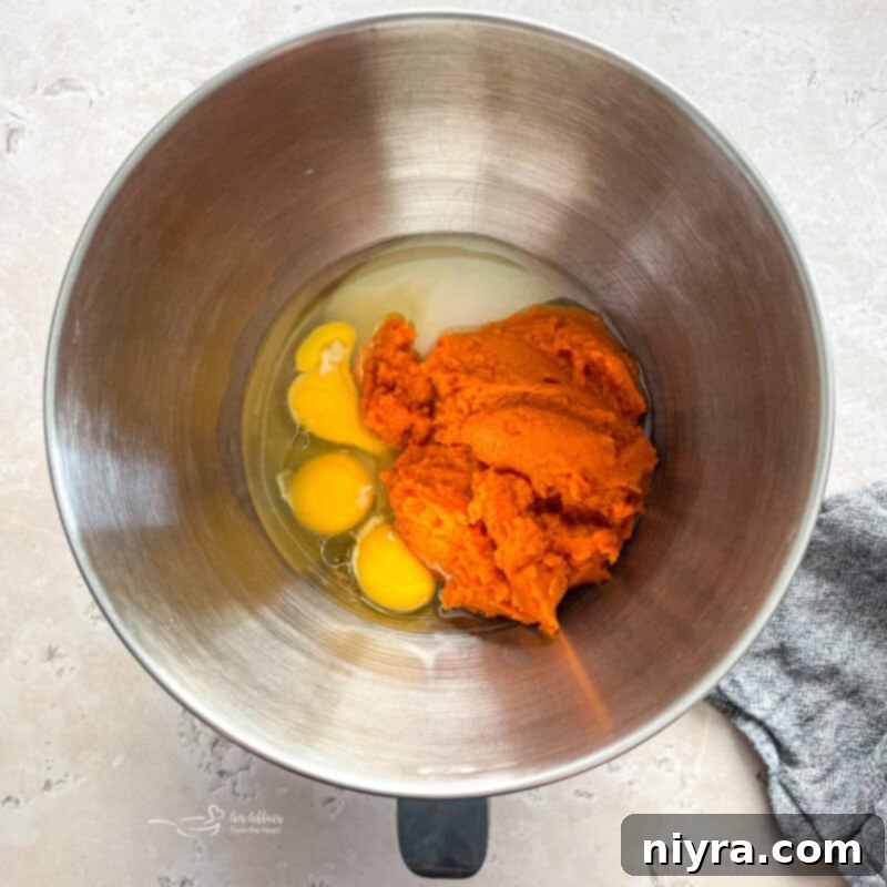 Mixing pumpkin, oil, eggs, and sugar together in a stand mixer bowl