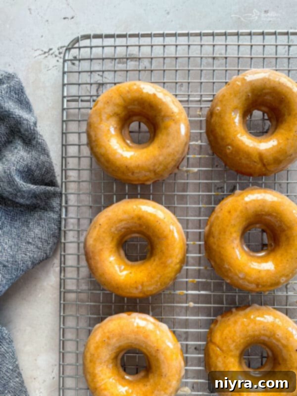 Dunking a warm baked pumpkin donut into a bowl of spiced glaze