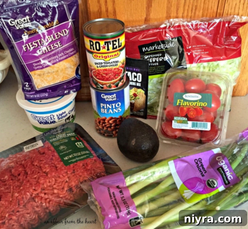 Loaded Tater Tot Taco Bake 5 Simple ingredients laid out for Taco Tot Casserole preparation on a kitchen counter: ground beef, RO*TEL, tater tots, cheese, and onion.