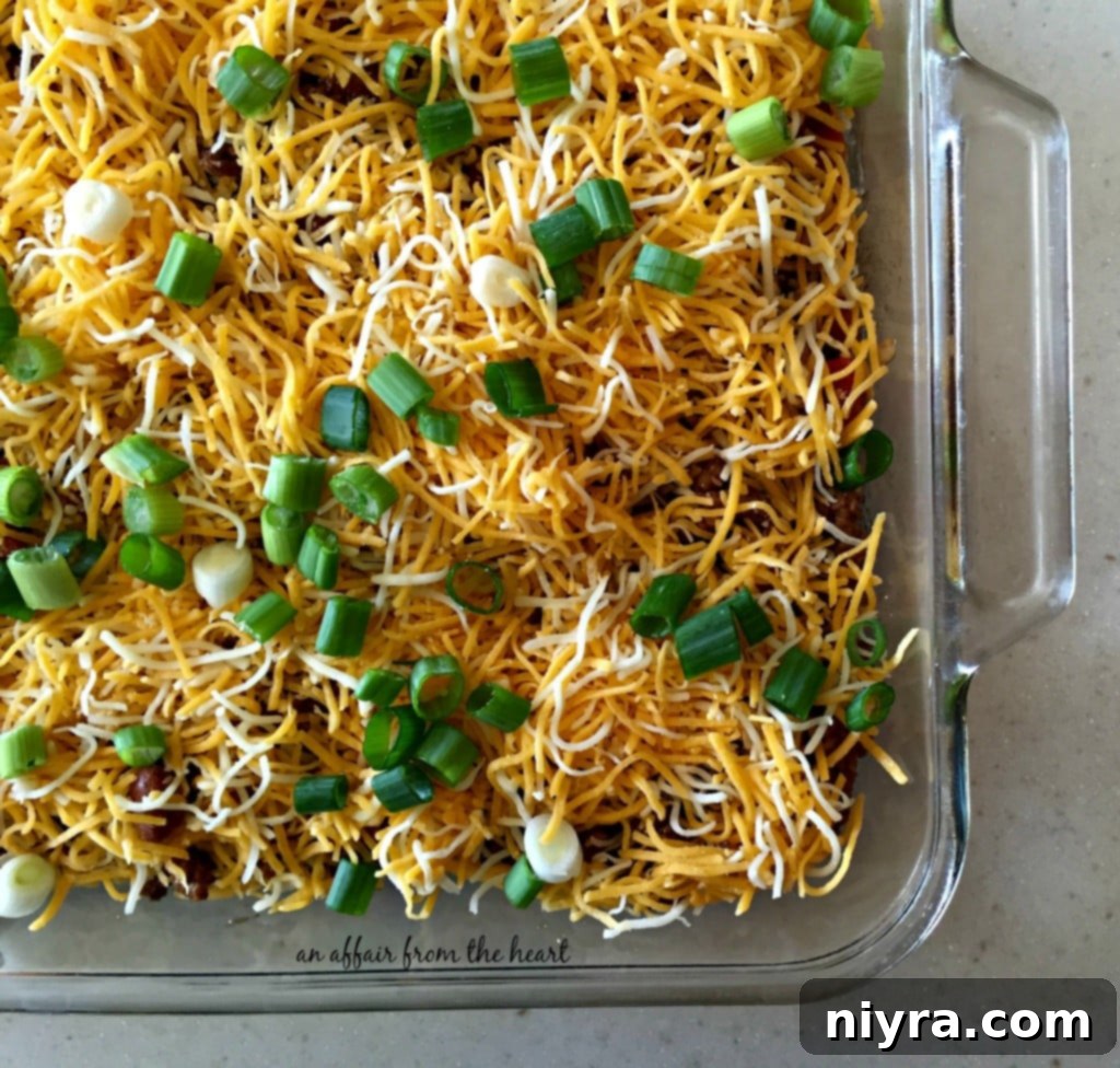 Loaded Tater Tot Taco Bake 8 Shredded Mexican cheese and sliced green onions beautifully topping the beef and bean mixture in the casserole dish.