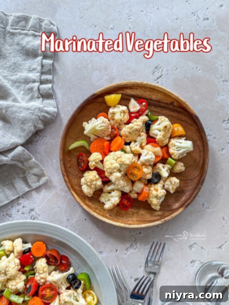 A large clear bowl of colorful Marinated Vegetables on a wooden table.
