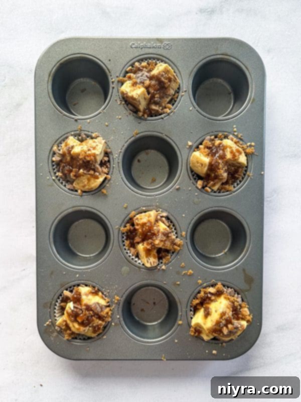 Muffin cups with cinnamon roll pieces, toffee, and brown sugar, now with melted butter drizzled over.