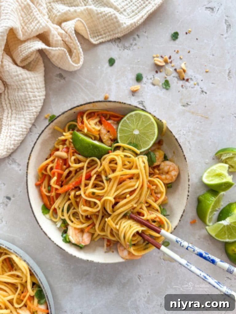 Overhead view of a white bowl filled with One-Pot Pad Thai, garnished with lime and peanuts.