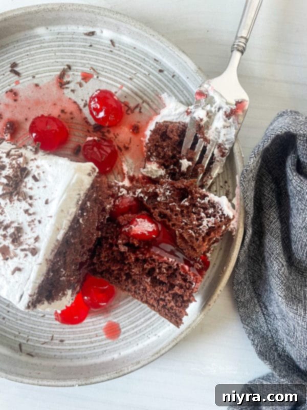 A perfectly portioned slice of Black Forest Cake on a plate with a fork, showing the creamy white frosting and moist cake layers.