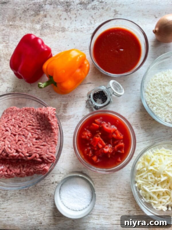 A large skillet filled with the raw ingredients for Stuffed Pepper Skillet: ground beef, chopped onions, bell peppers, tomatoes, and rice, before cooking.