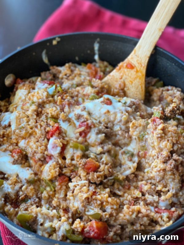 A large cast iron skillet filled with a cooked Stuffed Pepper Skillet meal, featuring visible bell peppers, ground beef, rice, and melted cheese, ready to serve.