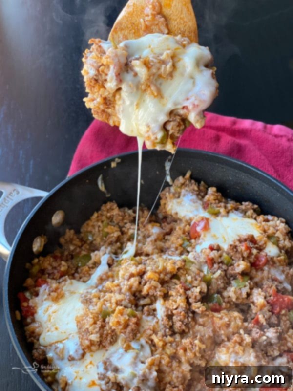 A close-up of a serving of Stuffed Pepper Skillet in a bowl, with a fork lifting a string of melted cheese, showcasing the delicious texture.