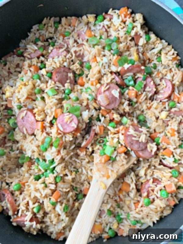 A close-up shot of Kielbasa Fried Rice, showing pieces of kielbasa, rice, peas, and carrots, in a skillet.