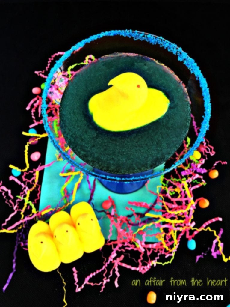 Close-up of a festive Peep Tart Martini, showcasing its blue hue and sugary rim, with another Peep chick on the side.