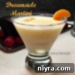 Dreamsicle martini in a martini glass garnished with an orange slice on a white surface.