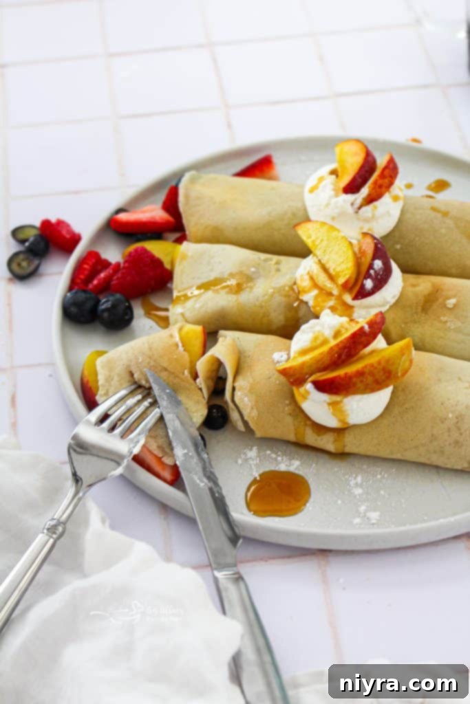 Beautifully plated sweet crepes filled with fresh strawberries, blueberries, raspberries, and peaches, topped with a dollop of whipped cream.