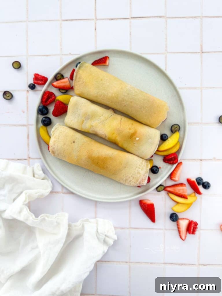 Close-up of a rolled sweet crepe on a white plate, topped with whipped cream and mixed berries.