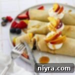 Using a fork and knife to take a bite out of a sweet crepe with summer fruit.