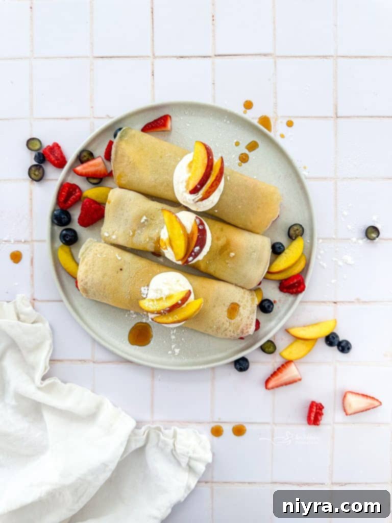 A plate of two rolled sweet crepes, garnished with fresh mixed berries and a dusting of powdered sugar, with a fork ready to enjoy.