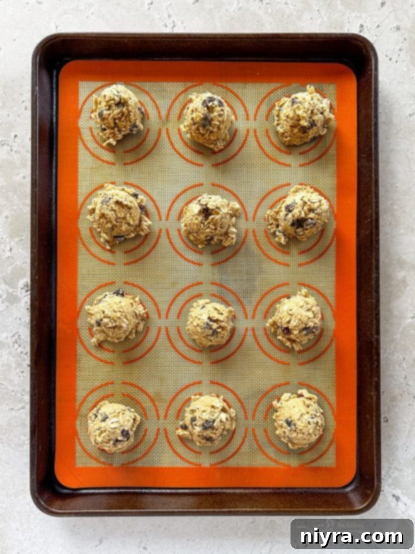 Close-up of oatmeal raisin cookie dough being scooped onto a parchment-lined baking sheet.