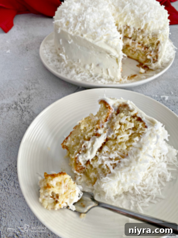 A slice of Coconut Cream Poke Cake with a fork, showing the moist layers and coconut whipped cream frosting, on a white plate.