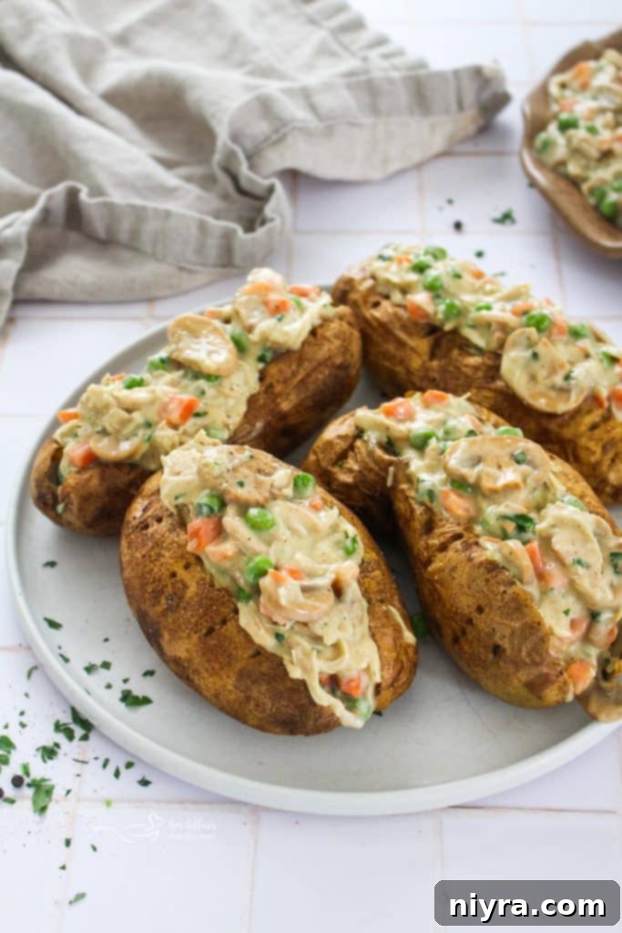 Two Chicken à la King Baked Potatoes on a wooden board, garnished with fresh parsley.