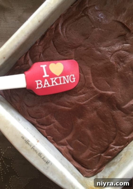 Thick brownie batter being pressed into a baking pan