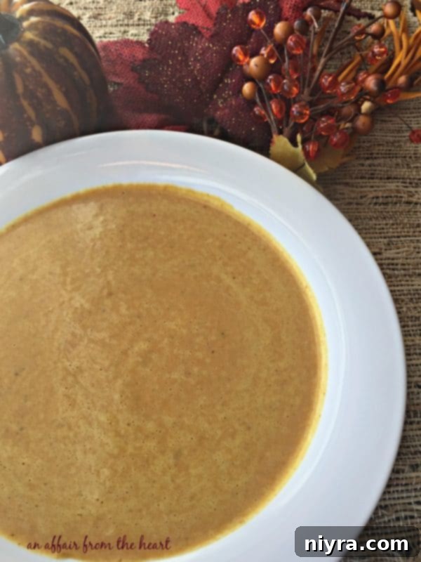 Overhead shot of a bowl of creamy pumpkin curry soup with a spoon, ready to eat.