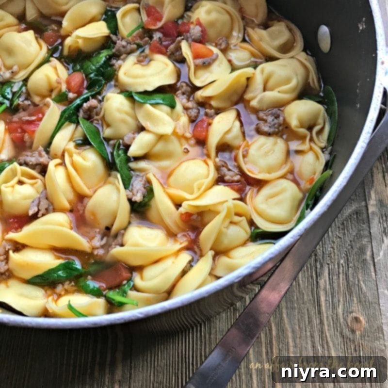 Tortellini Soup with Spinach and Sausage in a white bowl with a spoon.