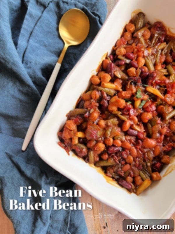 A wide shot of the Five Bean Baked Beans in a large casserole dish, with fresh bread and greens, depicting a complete meal.