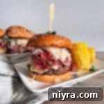 Pastrami Burger with Kraut on a white plate with corn and with burgers behind it