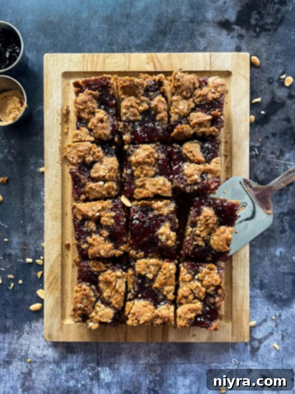 Close-up of a stack of PB&J Oatmeal Cookie Bars on a wooden plate, with a knife in the background