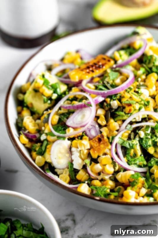 A bowl of Grilled Corn and Avocado Salad presented on a rustic wooden table with a fork, ready to be enjoyed