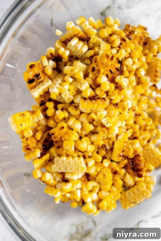 Step 2: A sharp knife carefully removing charred corn kernels from a grilled cob into a large mixing bowl