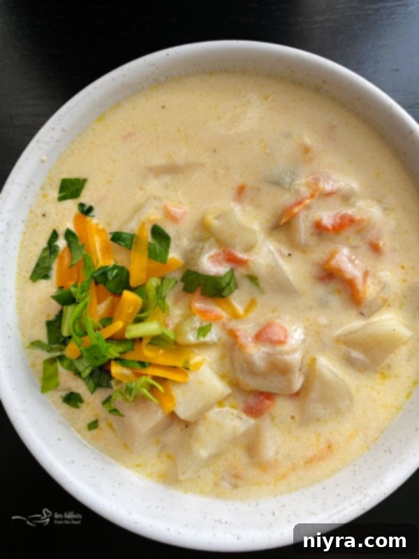 Top view of cheesy potato soup in white bowl, garnished with fresh herbs and a swirl of cream.