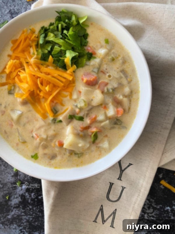 Close-up view of cheesy potato soup in a white bowl, garnished with shredded cheese and fresh parsley.
