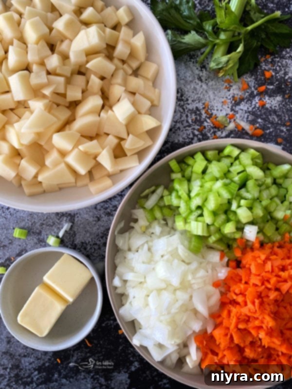 Assorted fresh ingredients including chopped potatoes, onions, celery, carrots, and a stick of butter, arranged on a rustic surface.