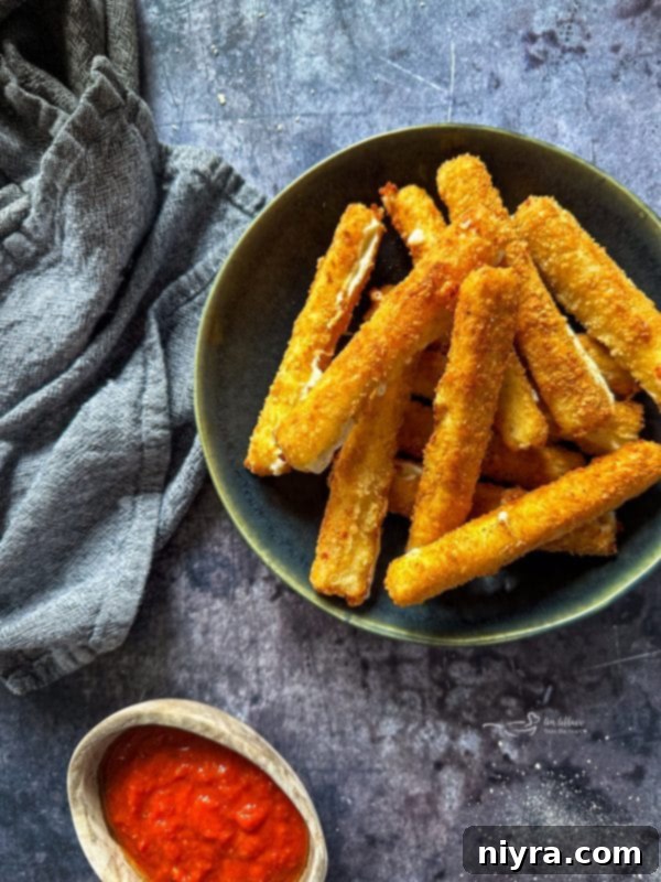 A plate of freshly fried homemade mozzarella sticks, served with a side of warm marinara sauce for dipping.